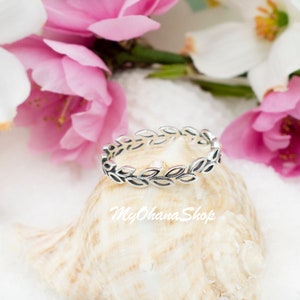 May include: A silver ring with a delicate leaf design. The ring is on a seashell with pink flowers in the background.