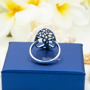 May include: A silver ring with a tree of life design. The ring has an oval-shaped centerpiece with a detailed tree silhouette. The band is smooth and polished. The ring is set on a blue box with the text "MyOhanShop".