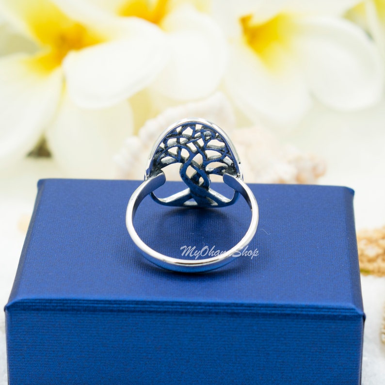 May include: A silver ring with a tree of life design. The ring has an oval-shaped centerpiece with a detailed tree silhouette. The band is smooth and polished. The ring is set on a blue box with the text "MyOhanShop".