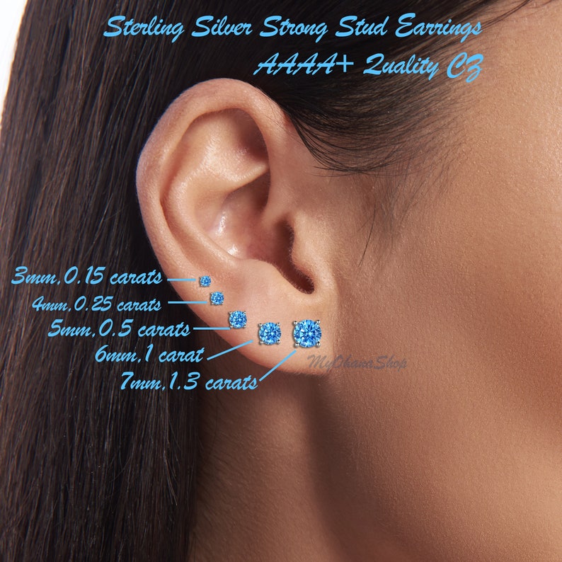 May include: Close-up of a person's ear with five different sizes of sterling silver stud earrings with blue cubic zirconia stones. The earrings are labeled with their size in millimeters and carat weight. The text "Sterling Silver Strong Stud Earrings AAAA+ Quality CZ" is visible at the top of the image.
