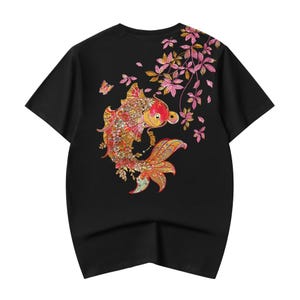 May include: A black short-sleeve t-shirt featuring a large, detailed graphic of a koi fish on the back. The fish is rendered in shades of red, orange, and gold with intricate floral patterns. Pink leaves and a small butterfly surround the fish.