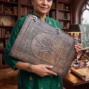 May include: A large, rectangular, dark brown leather-bound book featuring an embossed tree design on the front cover, intricate Celtic knotwork borders, and three metallic latches along the side to secure the pages closed.