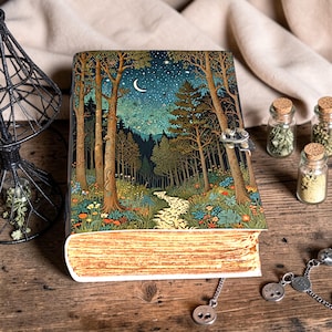 May include: A hardcover journal with a forest scene cover. The cover features a detailed illustration of a moonlit forest with a path, trees, and flowers. The journal has a metal clasp and a decorative bookmark.