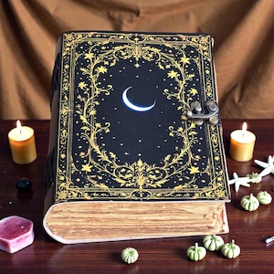 May include: A dark blue leather-bound journal with a crescent moon and star design. The cover features gold floral and celestial accents. The journal has a metal clasp and aged paper pages, evoking a vintage or fantasy theme.