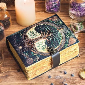 Op de afbeelding: Een leren gebonden dagboek met een levensboomontwerp op de omslag. De omslag is donkergroen met gouden accenten en een metalen sluiting. De pagina's zijn verouderd. Het dagboek ligt op een houten oppervlak met kaarsen en kleine flesjes.