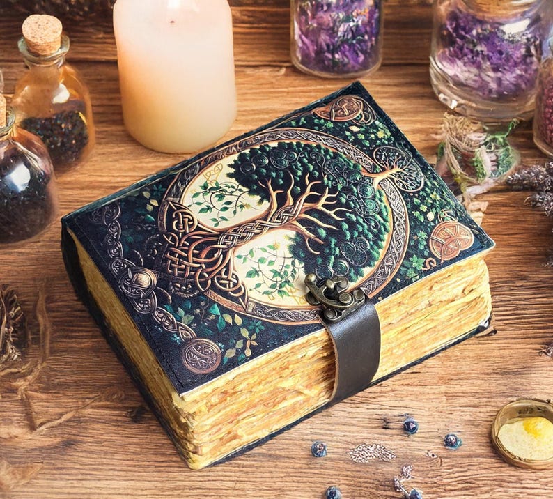 Op de afbeelding: Een leren gebonden dagboek met een levensboomontwerp op de omslag. De omslag is donkergroen met gouden accenten en een metalen sluiting. De pagina's zijn verouderd. Het dagboek ligt op een houten oppervlak met kaarsen en kleine flesjes.