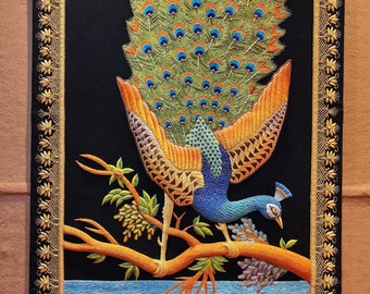 Puede incluir: Un pavo real bordado de colores con sus plumas de la cola extendidas, posado en una rama con hojas verdes. El pavo real está rodeado de un marco dorado con un diseño floral.