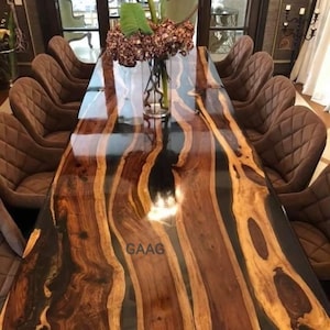May include: A long, rectangular dining table with a dark wood top and black epoxy resin inlay. The table has a high gloss finish and is surrounded by brown leather chairs. The table is set with a vase of pink flowers.
