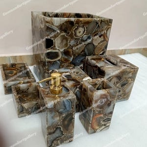 May include: A bathroom set made of agate stone with a brown, gray, and white color scheme. The set includes a soap dispenser, toothbrush holder, tumbler, and two small trays.