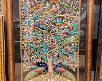 Puede incluir: Una obra de arte bordada enmarcada que representa un árbol colorido con pájaros y pavos reales. El árbol está rodeado de flores y hojas. La obra de arte está enmarcada en un marco dorado y marrón. El texto "GAAG" es visible en la parte inferior de la obra de arte.