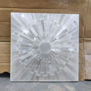 Pode incluir: Uma placa de carregamento de selenita branca com um design circular de pontos radiantes. A placa tem aproximadamente 15 cm de diâmetro e é feita de cristal de selenita natural.
