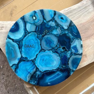 Puede incluir: Una bandeja decorativa circular compuesta por rodajas de ágata azul pulida en tonos variados de azul, marino y cian. La superficie presenta un mosaico de patrones de piedra natural con bandas concéntricas y el texto GAAG a la izquierda.