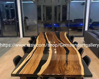 May include: A large, rectangular dining table with a live edge design. The tabletop features alternating bands of light and dark wood, with black resin filling the gaps. The table is supported by a black base and surrounded by black chairs.