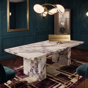 Op de afbeelding: Een rechthoekige eettafel met een gepolijst wit en paars marmeren blad en een bijpassende gecanneleerde marmeren voet. Een goudkleurig rechthoekig plaatje met de tekst GemsAndArtGallery is in het midden van het tafeloppervlak geplaatst.