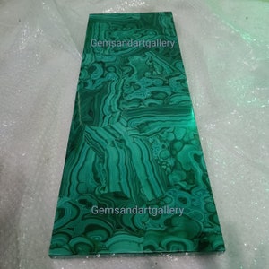 May include: A green malachite slab with a swirling pattern. The slab is rectangular and has a smooth surface. The text "Gemsandartgallery" appears twice on the slab.