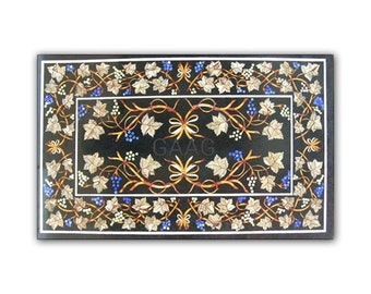 May include: A black marble table top with a decorative inlay of a vine pattern in gold, white, and blue. The inlay features leaves, grapes, and bows.
