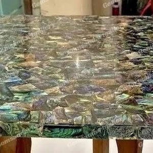 May include: A rectangular table with a mosaic top. The surface is made of iridescent, multi-coloured pieces, creating a shimmering effect. The table has wooden legs.