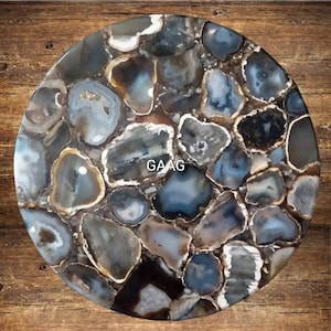 May include: A round table top made of agate stone. The table top is a mosaic of different sized and shaped agate pieces in shades of gray, brown, and white. The agate pieces have a natural, polished finish. The table top is approximately 30 inches in diameter.