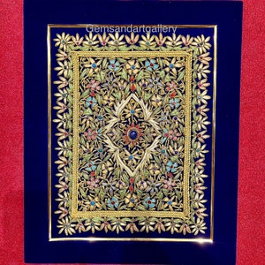 Puede incluir: Una obra de arte enmarcada con un fondo de terciopelo azul y un diseño dorado con intrincados patrones florales y piedras preciosas de colores. La obra de arte se titula "Gemsandartgallery".