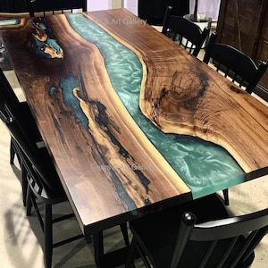 May include: A large wooden table with a live edge and a turquoise blue epoxy river running down the center. The table is surrounded by black chairs.