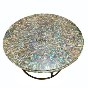 May include: Circular coffee table featuring a mosaic top in iridescent hues of blue, green, and gold. It has a dark metal base. The text "GAAG" is visible on the table's surface.