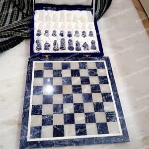 May include: A blue and white marble chess set. The chess board is a checkerboard pattern of blue and white squares. The chess pieces are blue and white, and are stored in a blue velvet lined box.