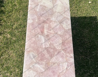 May include: A pink and white rose quartz table top with a natural, irregular, and textured surface. The table top is made of many pieces of rose quartz that have been glued together.