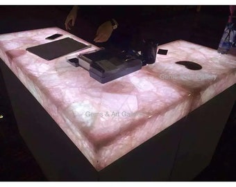 May include: A large, rectangular countertop made of pink quartz with a white, glowing light underneath. The countertop is lit from below, highlighting the natural patterns and textures of the quartz. The countertop is perfect for a retail store or a home bar.