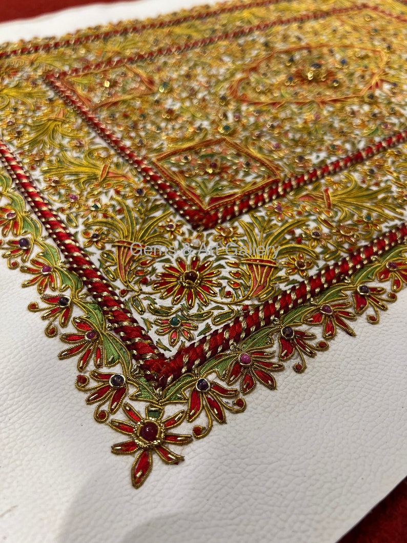 Puede incluir: Un fondo de cuero blanco con un dise&ntilde;o bordado en rojo, dorado y verde. El dise&ntilde;o presenta intrincados patrones florales y peque&ntilde;as piedras preciosas.