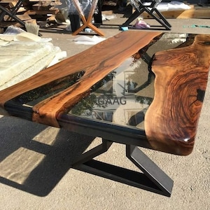 Peut inclure: Une table basse rectangulaire en bois avec un design à bord brut. La table présente un plateau en bois brun foncé avec une incrustation de résine époxy transparente et un piètement en métal noir. Dimensions : environ 152 cm de long, 76 cm de large et 46 cm de haut.