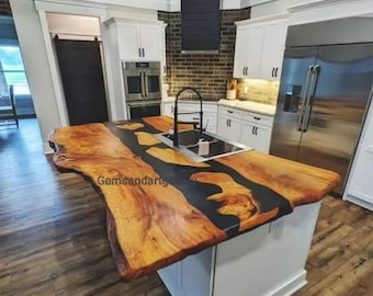 May include: A large, live edge wooden countertop with a black epoxy river running through the center. The countertop is in a modern kitchen with white cabinets and stainless steel appliances.