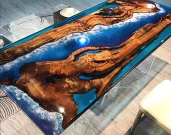 May include: A rectangular coffee table featuring two large, natural-edged wood slabs separated by a central river of translucent blue resin. The resin includes white, wave-like patterns, and the wood displays a rich, brown, swirling grain.