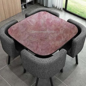 May include: A pink and white marble table top with four grey chairs. The table top has a unique marbled pattern and the chairs are upholstered in a grey fabric.