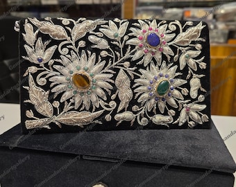 May include: A black velvet box with a silver and gemstone floral design. The box is closed and has a silver clasp.