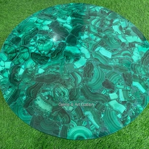 May include: A round table top made of green malachite stone. The table top is made of many small pieces of malachite that have been cut and polished to create a smooth surface. The table top is a beautiful example of the natural beauty of malachite.