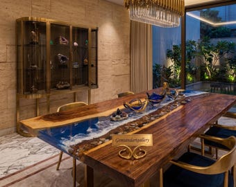 May include: A live-edge wooden dining table featuring a central resin inlay that mimics a beach shoreline with blue water, white waves, and pebbles. A gold-toned sign with the text Gemsandartgallery sits on the table surface.