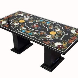 Puede incluir: Una mesa de comedor de mármol negro con un diseño de incrustaciones florales. La mesa tiene dos patas negras y una tapa rectangular.