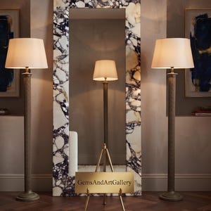 May include: A tall rectangular floor mirror with a frame featuring a white and dark purple marbled stone pattern. In front of the mirror stands a small gold-toned metal easel holding a rectangular sign with the text GemsAndArtGallery.