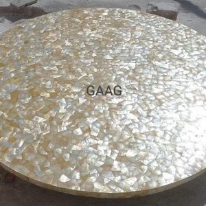 May include: A round table top made of white and gold mother of pearl tiles. The table top is approximately 3 feet in diameter. The text "GAAG" is visible in the center of the table top.