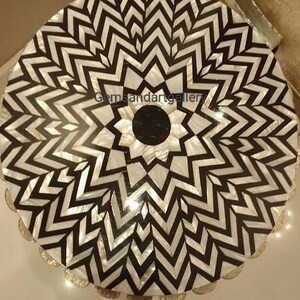 以下が含まれることがあります： 黒と白の真珠貝の象嵌細工で作られた丸いテーブルトップ。テーブルトップは、黒と白の三角形の幾何学模様が特徴です。