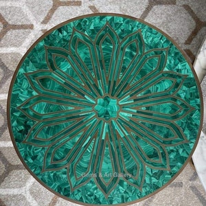Può includere: Un piano da tavolo rotondo con un design di intarsi in malachite verde. Il design presenta un grande fiore con dettagli intricati. Il piano del tavolo è circondato da un bordo in ottone. "Gems & Art Gallery" è stampato sul piano del tavolo.