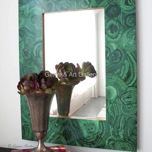 May include: A rectangular mirror with a green malachite frame. The frame is made of small pieces of malachite that are arranged in a geometric pattern. The mirror is reflecting a room with a window and two vases with flowers.