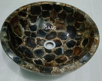 May include: A brown agate stone sink with a white drain. The sink is made of many small pieces of agate that have been glued together. The sink is round and has a smooth finish. The sink is labeled "GAAG".