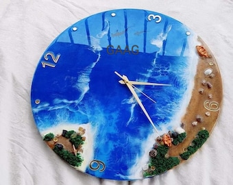 Può includere: Un orologio in resina blu e marrone con una scena di spiaggia. Il quadrante dell'orologio ha numeri bianchi e lancette dorate. La scena della spiaggia include sabbia bianca, acqua blu e piccole conchiglie.