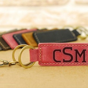 May include: A pink leather keychain with a brass key ring and a snap hook. The keychain has the initials "CSM" embossed in black.