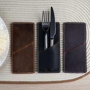 May include: Three leather place card holders with stitched edges. The center holder has a silver fork and knife inside.