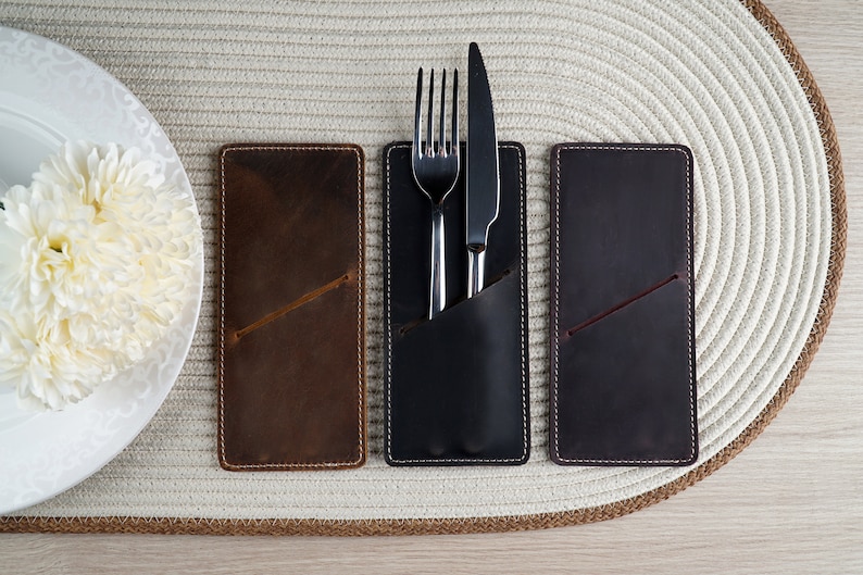 May include: Three leather place card holders with stitched edges. The center holder has a silver fork and knife inside.