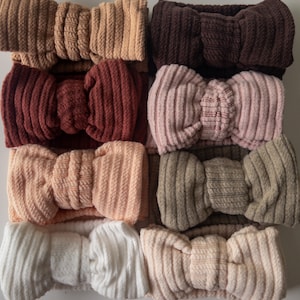 May include: Set of eight headbands in various colours and textures. The headbands are made from a soft, stretchy material and feature a bow detail. The colours include brown, pink, beige, and white.