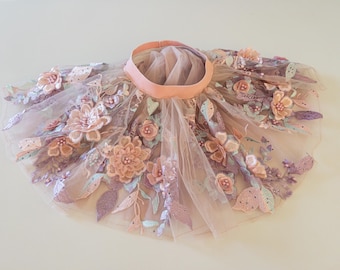 May include: A delicate tulle skirt with floral embroidery in shades of pink, lavender, and green. The skirt has a wide waistband and a flowing, layered design.