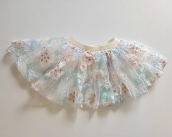 May include: A white tulle skirt with a floral pattern in shades of blue, pink, and green. The skirt has a gathered waistband and a scalloped hem.